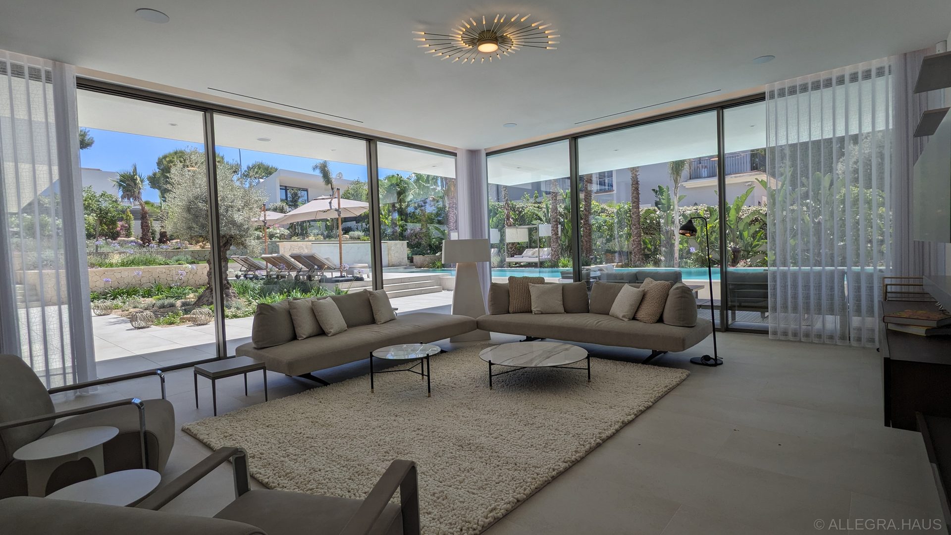 ALLEGRA Wohnzimmer mit Kamin, raumhohen Schüco-Fensterfronten und Blick auf den Pool